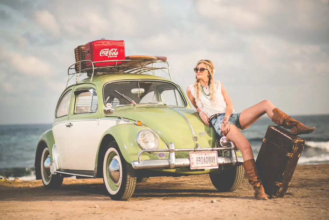 Woman Volkswagen Beach by Hydrofoiling woman leaning on green and white Volkswagen Beetle near sea under white sky during daytime