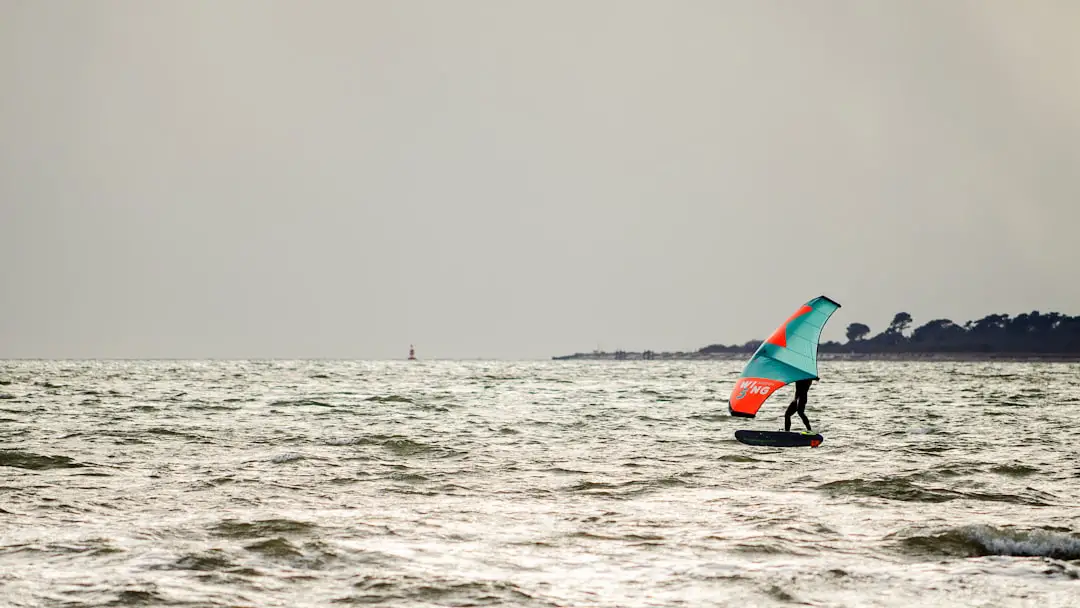 person in black wet suit riding red and black surfboard on sea during daytime
